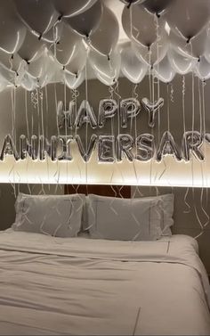 a bed with white sheets and balloons hanging from the ceiling above it that says happy anniversary