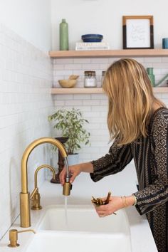 a woman is washing her hands in the kitchen sink while she stands next to the faucet