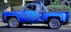 an old blue truck parked on the side of the road in front of a house