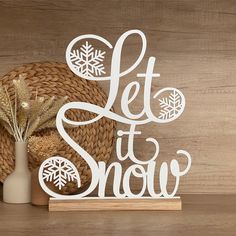 a wooden sign that says let it snow next to a vase with dried flowers and an ornament