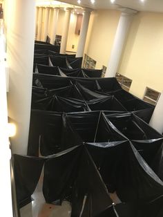 several black umbrellas are lined up on the floor in a room with columns and pillars