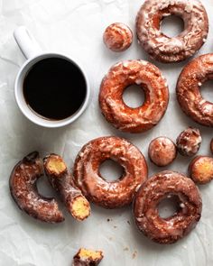 doughnuts and coffee sitting on top of a white tablecloth next to each other