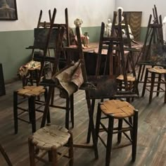 several wooden chairs and stools in a room with paintings on the wall behind them