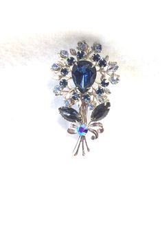 This flower brooch is done with light and dark blue stones.  The metal is done in a silver tone finish.  The size of the brooch is 2 1/2 x 1 1/2.  Overall condition of this brooch is good. Please read my policies on lost or stolen items. Blue Flower-shaped Jewelry Brooch, Blue Floral Brooch Jewelry, Formal Blue Flower Brooch, Formal Blue Flower Brooches, Green Brooch, Red Bud, Antique Gift, Blue Stones, Dress Clip