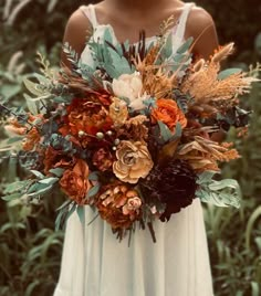 a woman in a white dress holding a bouquet of flowers and greenery on her wedding day