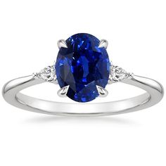 an oval shaped blue sapphire and diamond ring with two shoulders on the band, set in 18k white gold