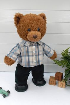 a brown teddy bear wearing a plaid shirt and black pants standing next to toy cars