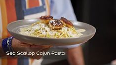 a man holding a plate of food with scallop cauliflower pasta on it