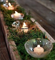 candles are lit in glass bowls with moss growing on the sides, along with greenery