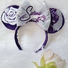 a purple and white minnie mouse ears with the word disney on it, sitting next to a flower