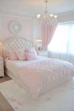 a bedroom with pink and white bedding, chandelier, rugs and curtains