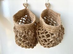 two crocheted baskets hanging from hooks on a white wall, one is brown and the other is beige