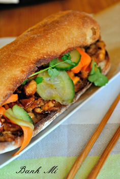 a sandwich with meat, vegetables and chopsticks on a white plate next to a green napkin