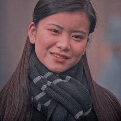 a woman with long hair wearing a scarf and smiling at the camera while standing in front of a gray background