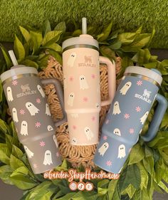 three coffee mugs sitting on top of a basket filled with green leaves and grass