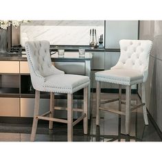 two white bar stools sitting next to each other in front of a kitchen counter