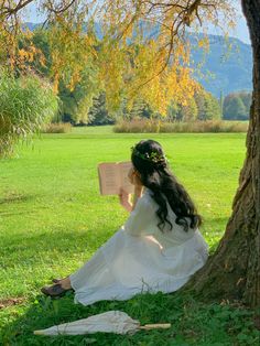 a woman sitting under a tree reading a book