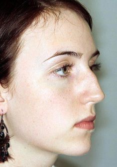 a close up of a person with earrings on their head and one eye open, looking off to the side