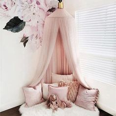 a canopy bed with pink pillows and flowers on the wall behind it, in front of a window