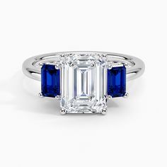 an emerald and blue sapphire engagement ring with three diamonds on the side, set in white gold