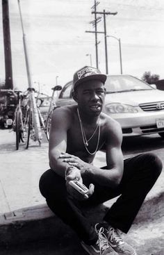 a man sitting on the curb with his skateboard in front of him and cars behind him