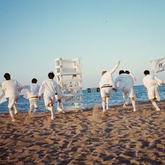 a group of men dressed in white running on the beach