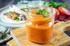 a jar filled with sauce sitting on top of a wooden cutting board next to other food