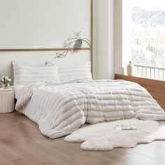 a large white bed sitting on top of a hard wood floor next to a window