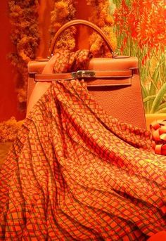 an orange and red blanket sitting on top of a table next to a purse with flowers in the background