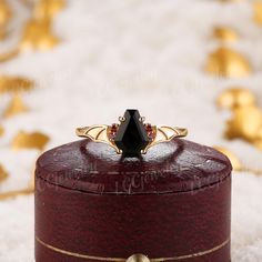 a black diamond ring sitting on top of a red velvet box with gold trimming