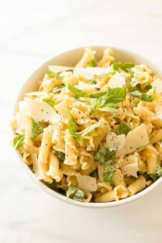 a white bowl filled with pasta and spinach on top of a marble countertop