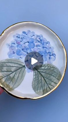 a hand holding a plate with blue flowers on the bottom and green leaves around it