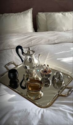 a tray that has some tea in it on top of a bed with white sheets