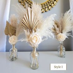 three vases with flowers and feathers in them on a table next to a mirror