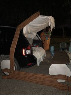 a car that is parked under a tent with the back door open and people standing around it