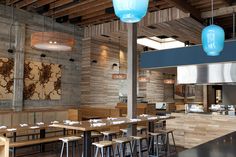 an empty restaurant with wooden tables and stools in the foreground, two blue lamps hanging from the ceiling