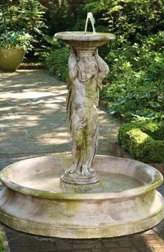 a fountain with a statue in the middle of it and bushes around it on either side