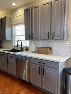 a kitchen with gray cabinets and white counter tops, stainless steel dishwasher in the middle