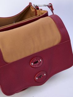 This red grained leather Postina Daily S bag boasts a fixed top handle, adjustable and detachable shoulder strap, turn-lock closure, and two main interior compartments. It also includes one interior zip pocket, one interior flat pocket, and a dust bag.    Dimensions: 12x5.9x7.4   Size nationality: UNI  Product code: 068010S0040000Z0940  Composition: 100% leather Daily Double Flap Satchel With Top Handle, Red Leather-lined Satchel For Travel, Red Satchel Briefcase With Top Carry Handle, Red Leather Briefcase With Top Carry Handle, Red Leather Briefcase With Top Handle, Red Textured Leather Top Handle Shoulder Bag, Business Red Shoulder Bag With Leather Lining, Red Leather Lined Shoulder Bag For Business, Red Leather-lined Shoulder Bag For Business