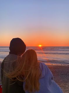 two people sitting on the beach watching the sunset