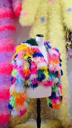 a mannequin wearing a colorful jacket in front of many other colored furs