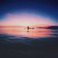 a person is swimming in the ocean at sunset or dawn with their back turned to the camera