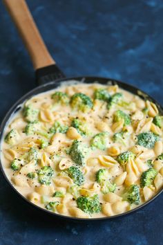 a skillet filled with pasta and broccoli on top of a blue table