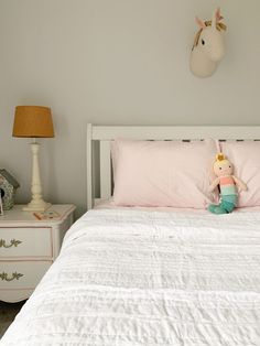 a white bed topped with a pink comforter next to a night stand and lamp