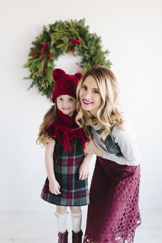 a woman and her daughter posing for a photo in front of a christmas wreath wearing matching outfits