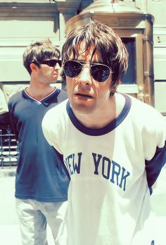 two young men walking down the street in front of a building, one with sunglasses on his head