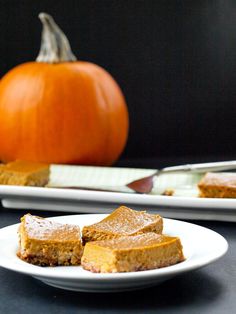 two plates with pieces of pumpkin pie on them next to a plate with a pumpkin in the background