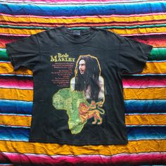 a black bob marley t - shirt laying on a multicolored blanket