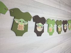 some baby yoda pictures hanging on a wall with clothes pins attached to it and paper cutouts in the shape of babies'faces