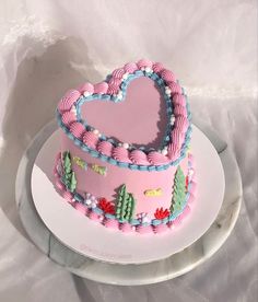 a pink heart shaped cake sitting on top of a white platter with frosting